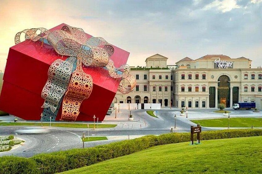 A large red gift box sculpture in front of a classical building with a dome and arched entrance. 2