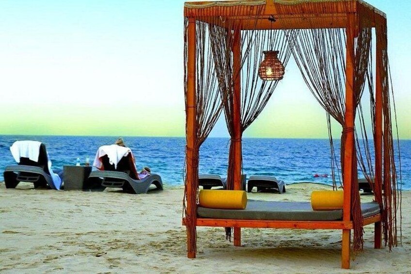 A beach with a wooden swing chair and lounge chairs. 5