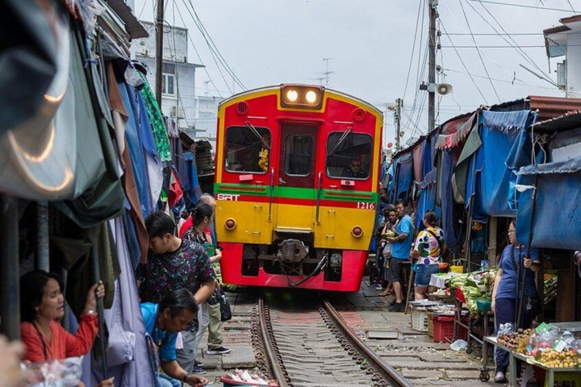 A train on tracks in a market area with people and stalls. 1