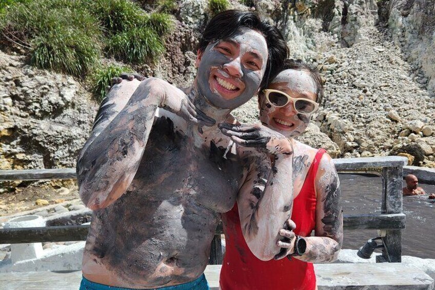Two people covered in mud, holding a fish, with rocky cliffs in the background. 1