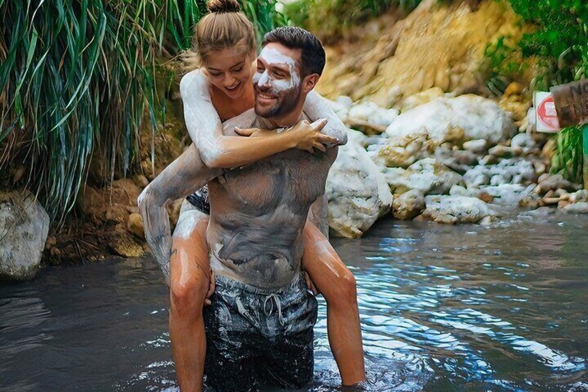 A man carrying a woman in a natural water setting with rocks and vegetation. 1
