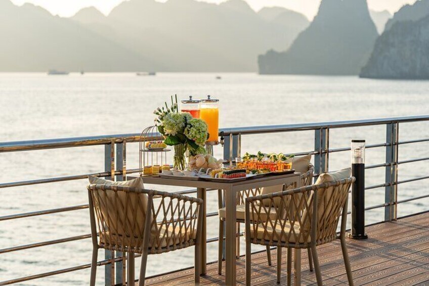 Une table avec des boissons et de la nourriture, placée sur une terrasse qui donne sur un plan d’eau, avec des montagnes en arrière-plan. 4