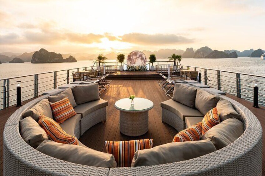 Un espace extérieur circulaire aménagé avec des canapés et une table centrale, installé sur une terrasse en bois et offrant une vue sur une étendue d’eau bordée d’îles lointaines. 5