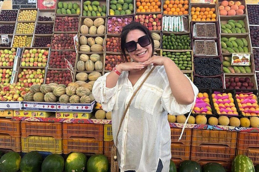 A person standing in front of a fruit and vegetable market with various produce displayed in crates. 5