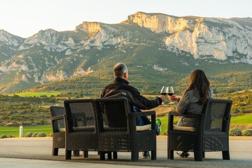 Two people sitting on wicker chairs facing a mountainous landscape. 1