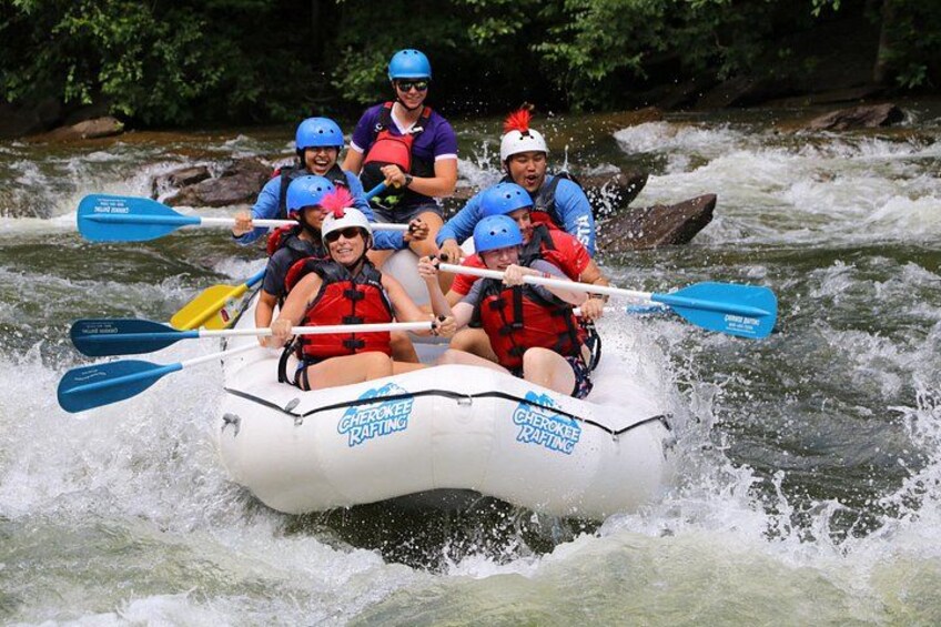Un grupo de personas haciendo rafting en un bote blanco con remos azules, rodeadas por un río. 2
