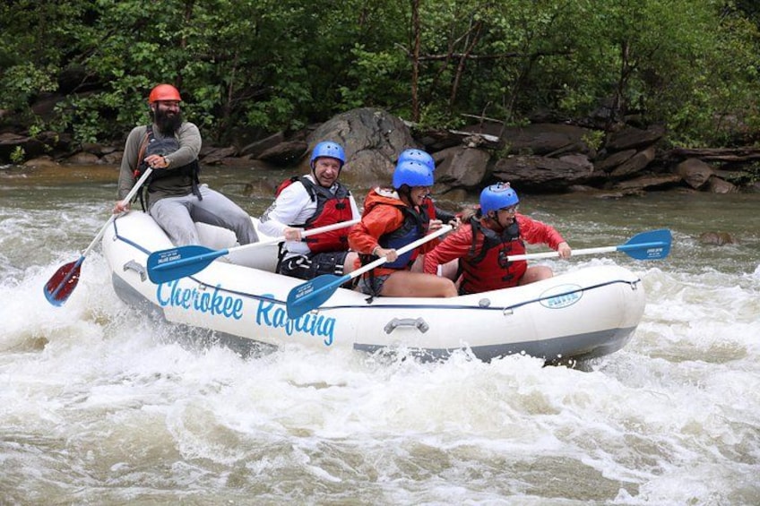 Een witte opblaasbare raft met de tekst 'Cherokee Rafting' erop, bewogen door vier mensen met helmen en reddingsvesten. 3