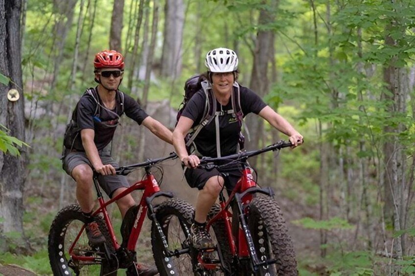 Two people on mountain bikes in a forested area. 1