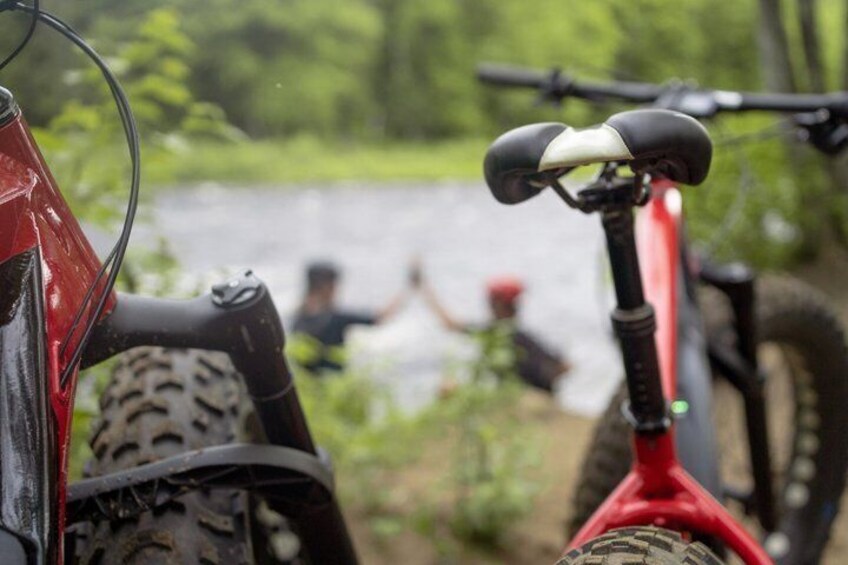 A mountain bike with a red frame and black tires, a person in the background, and a body of water. 5