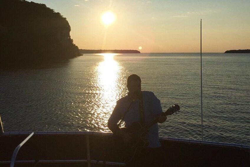 Una persona tocando la guitarra en un bote al atardecer. 2