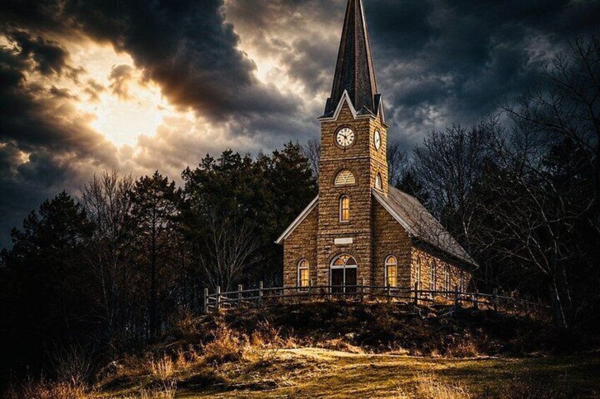 A church with a tall steeple and clock, surrounded by trees and a grassy area under a cloudy sky. 2
