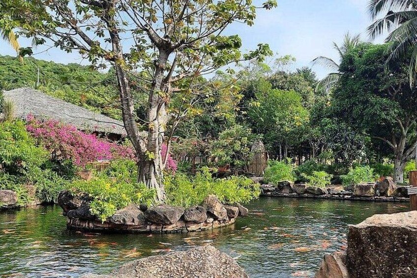 A tropical garden with a pond, rocks, and a thatched-roof structure. 5