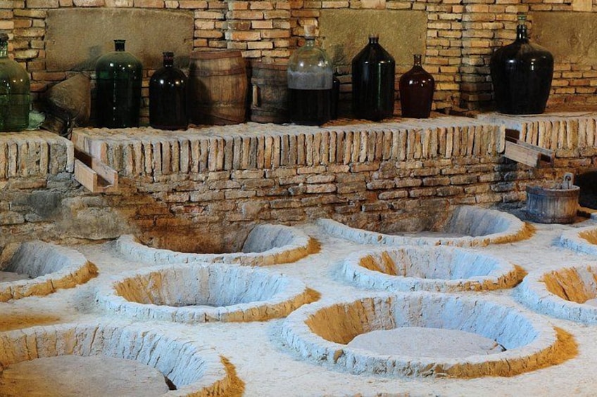 A traditional stone floor with circular basins, a brick wall, and various containers. 3