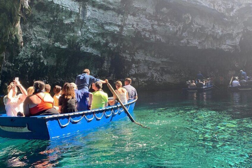Un grupo de personas en una bota azul remando por aguas cristalinas cerca de una cueva rocosa. 5