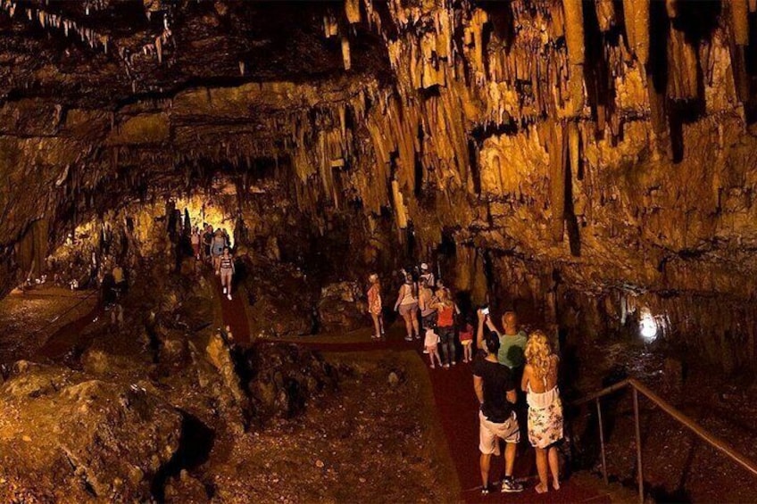 A cave with stalactites and a group of people walking on a path. 3
