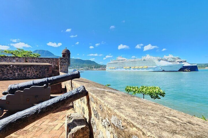 A cruise ship docked at a port with a stone wall and cannons in the foreground. 3