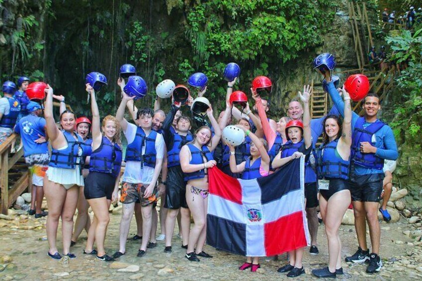 A group of people wearing life jackets and helmets, holding a flag, in a forested area. 5