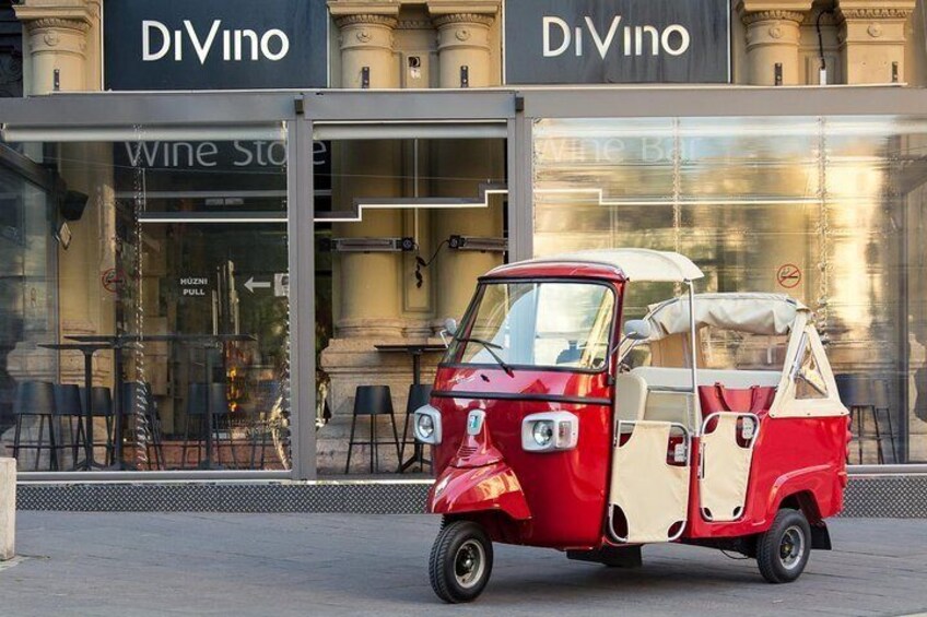 Een rode en witte oldtimer geparkeerd voor een gebouw met 'DiVino' aanduiding. 1