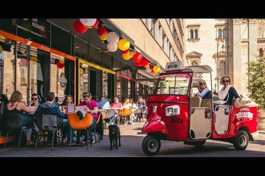 Een rode foodtruck geparkeerd voor een restaurant, waar mensen aan het dineren zijn. 2