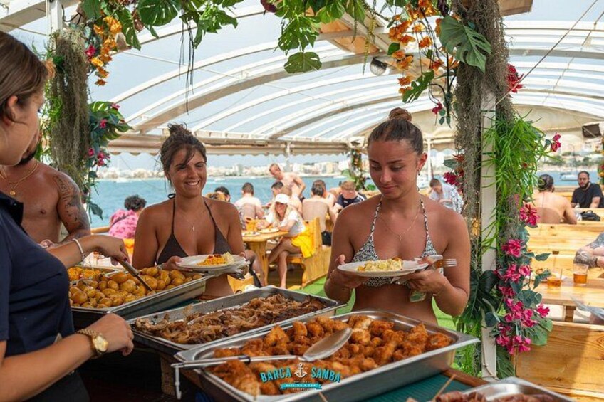 Ein Buffet mit verschiedenen Speisen, Personen beim Essen und ein Pool im Hintergrund. 1