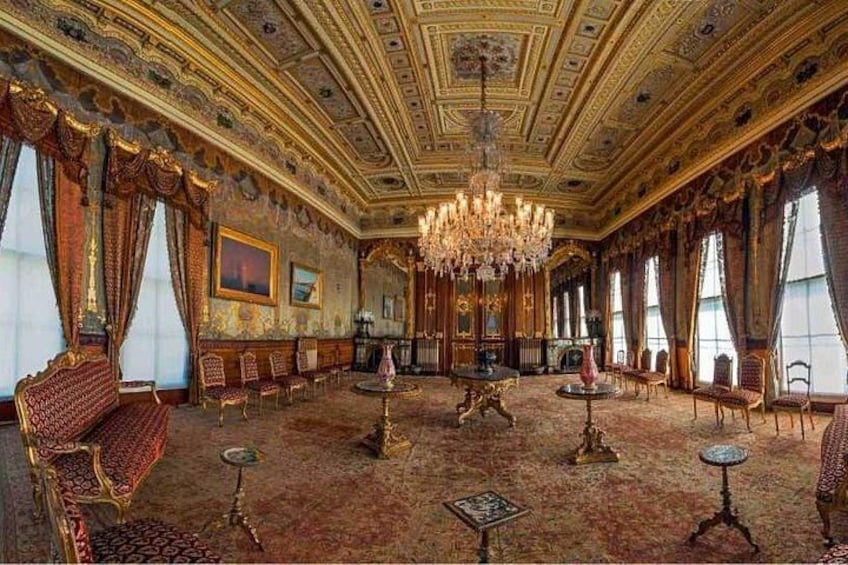 An opulent room with ornate chandeliers, red and gold furniture, and a patterned carpet. 3