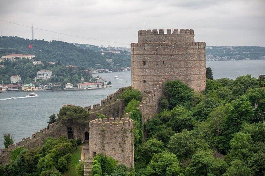 A historic stone castle with a tower overlooking a river, surrounded by lush greenery. 2