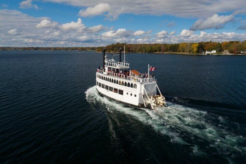 A white riverboat with multiple decks and flags, moving on a river with a forested shoreline in the background. 4