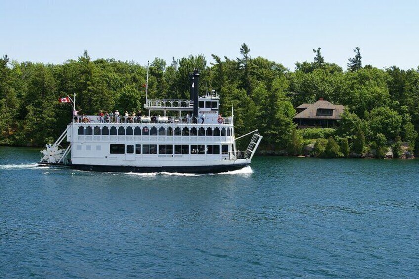 A white riverboat with multiple decks and passengers, moving on a river with a forested shoreline. 3