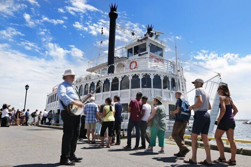 A steamboat with passengers and a man playing a banjo on the dock. 1