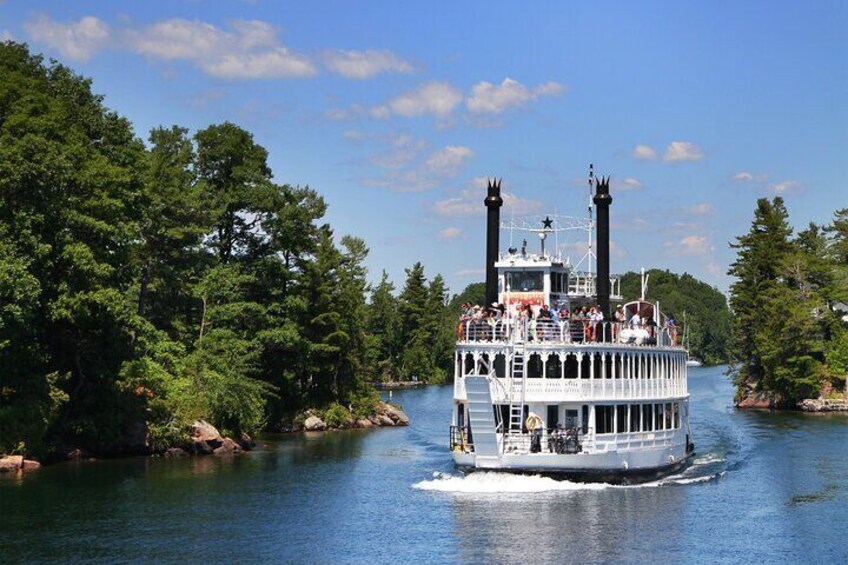 A steamboat with two tall chimneys, passengers, and a river surrounded by trees. 2
