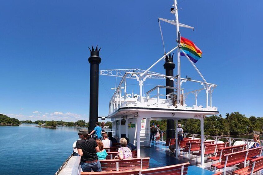 A boat with a black smokestack and a rainbow flag, passengers on the deck, and a clear blue sky. 5