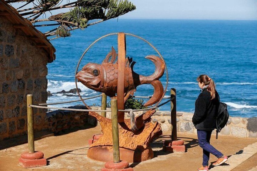 A coastal scene with a large metal sculpture of a fish, a wooden structure, and a person walking. 2