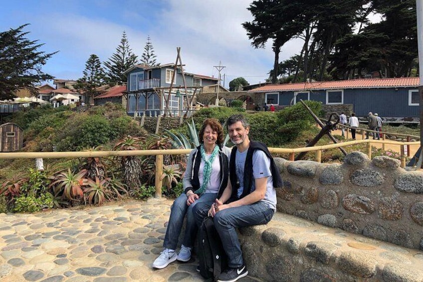 Two people sitting on a stone wall with a garden and buildings in the background. 4
