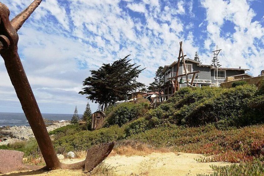 A coastal landscape with a house on a hillside, a sandy path, and a view of the ocean. 3