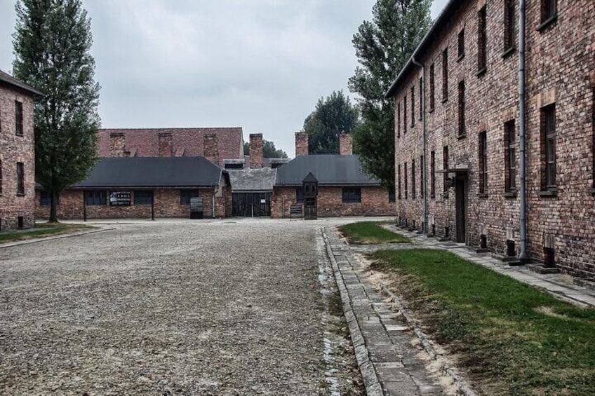 Une cour recouverte de gravier, bordée de bâtiments en briques, avec une zone herbeuse et des arbres. 4