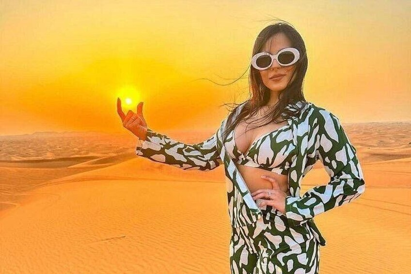 A person in a patterned outfit standing in a desert with sand dunes and a sunset in the background. 1