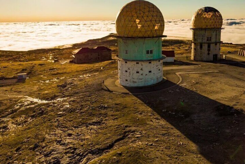 A coastal radar station with two large domes, surrounded by rocky terrain and a building in the background. 2