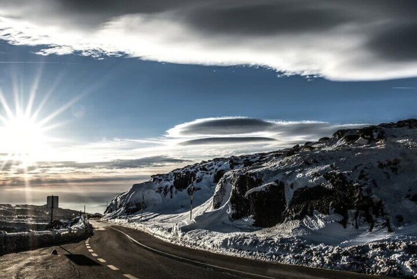 A snow-covered mountain road with the sun shining through clouds. 4