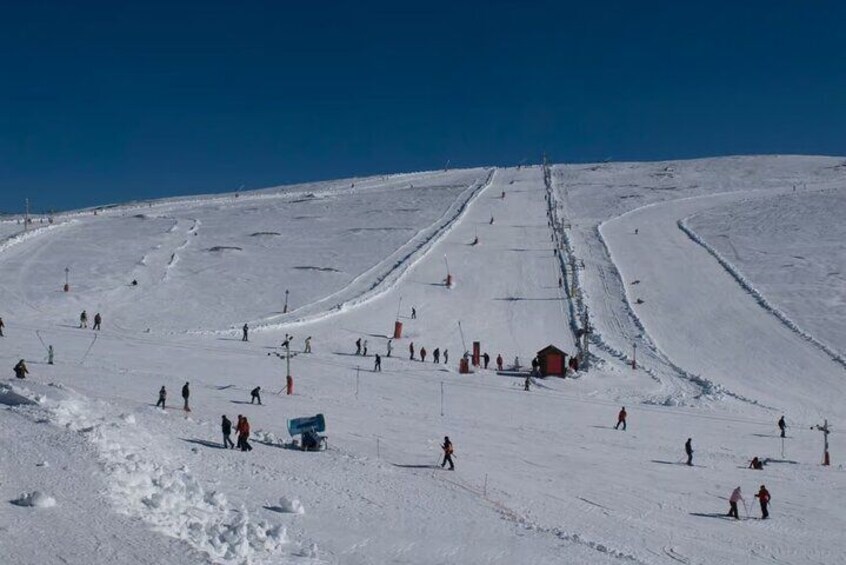 A snowy ski slope with skiers and a small red building. 5