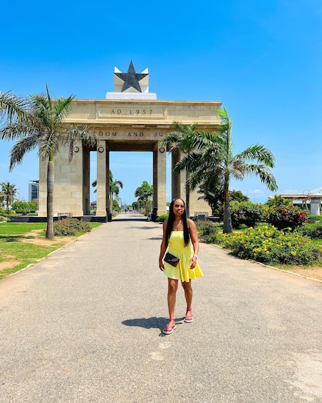 A woman in a yellow dress standing in front of a monument with a star on top and the inscription 'DOM AND JUS' visible. 2