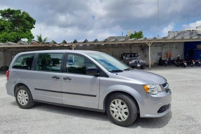 En sølvfarvet minivan parkeret på en parkeringsplads med en bygning og parkerede motorcykler i baggrunden. 5