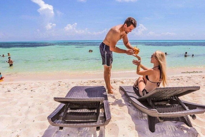 En strand med to liggestole, en person stående og en person siddende. 3