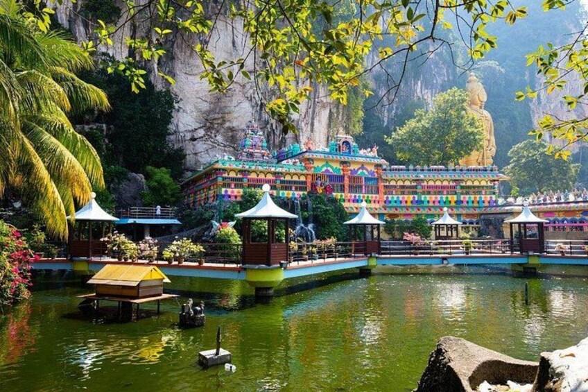 Ein farbenprächtiger Tempelkomplex mit einer großen Buddha-Statue, umgeben von Wasser und üppiger Vegetation. 5