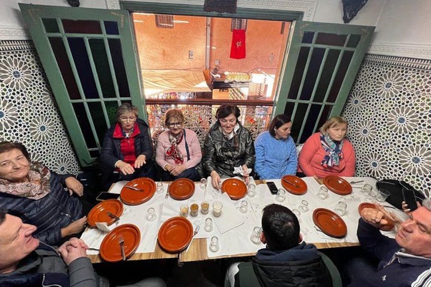 Een groep mensen zit rond een tafel met borden en glazen, in een kamer met behang. 5