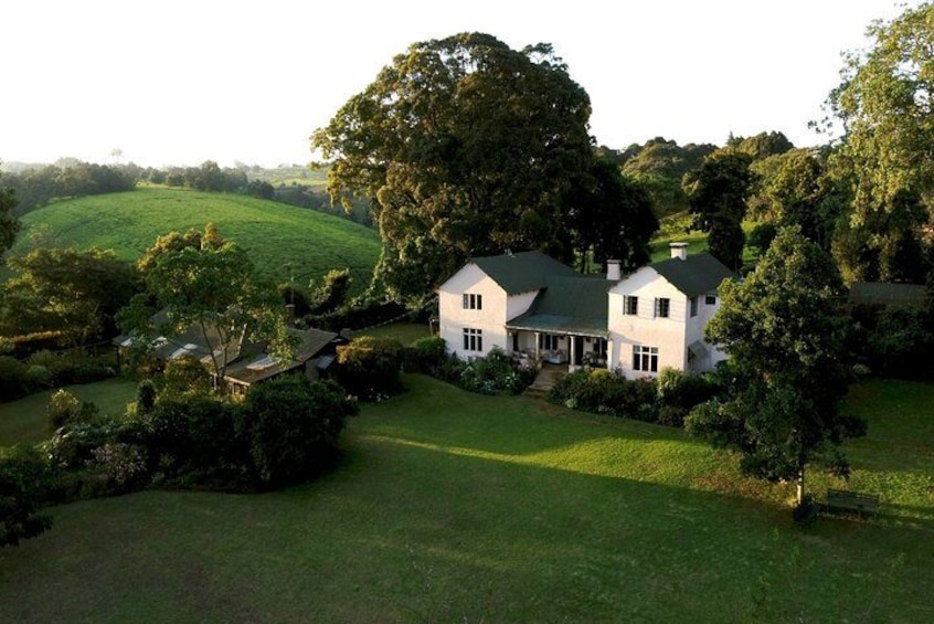 Een groot wit huis met een groen dak, omringd door weelderige begroeiing en glooiende heuvels. 2