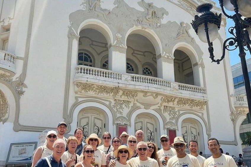 Un grupo de personas frente a un edificio blanco con arquitectura ornamentada, que incluye ventanas en arco y balcones decorativos. 2