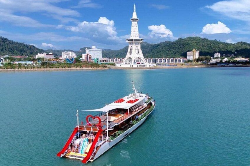 A large ferry with a red and white design, a white tower in the background, and a calm body of water. 1