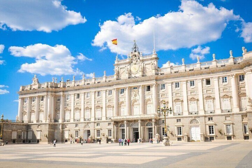 A large, ornate building with a flag, columns, and a wide plaza. 1