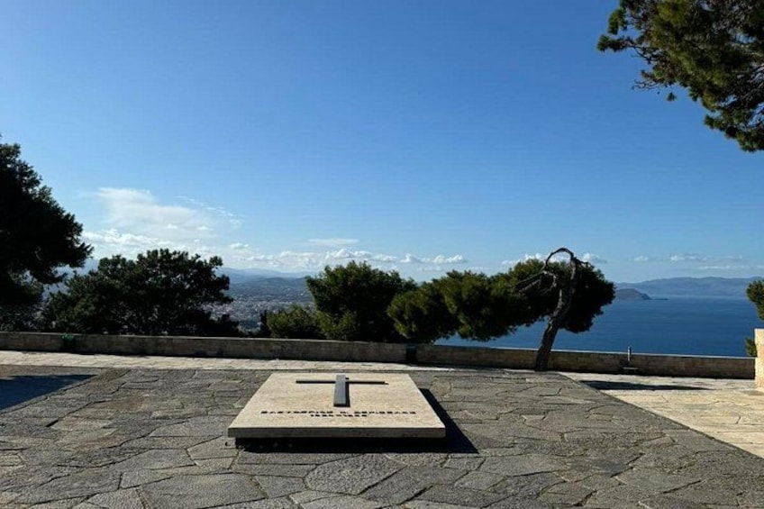 Una panca di pietra con una targa, un albero e vista sul mare e sulle montagne. 3
