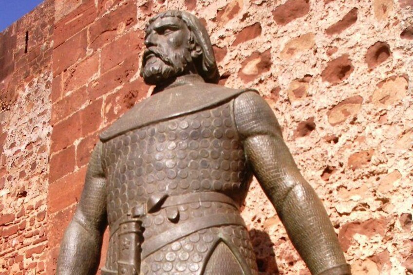 Una estatua de bronce de una figura histórica con armadura, de pie frente a un muro de ladrillo rojo. 3